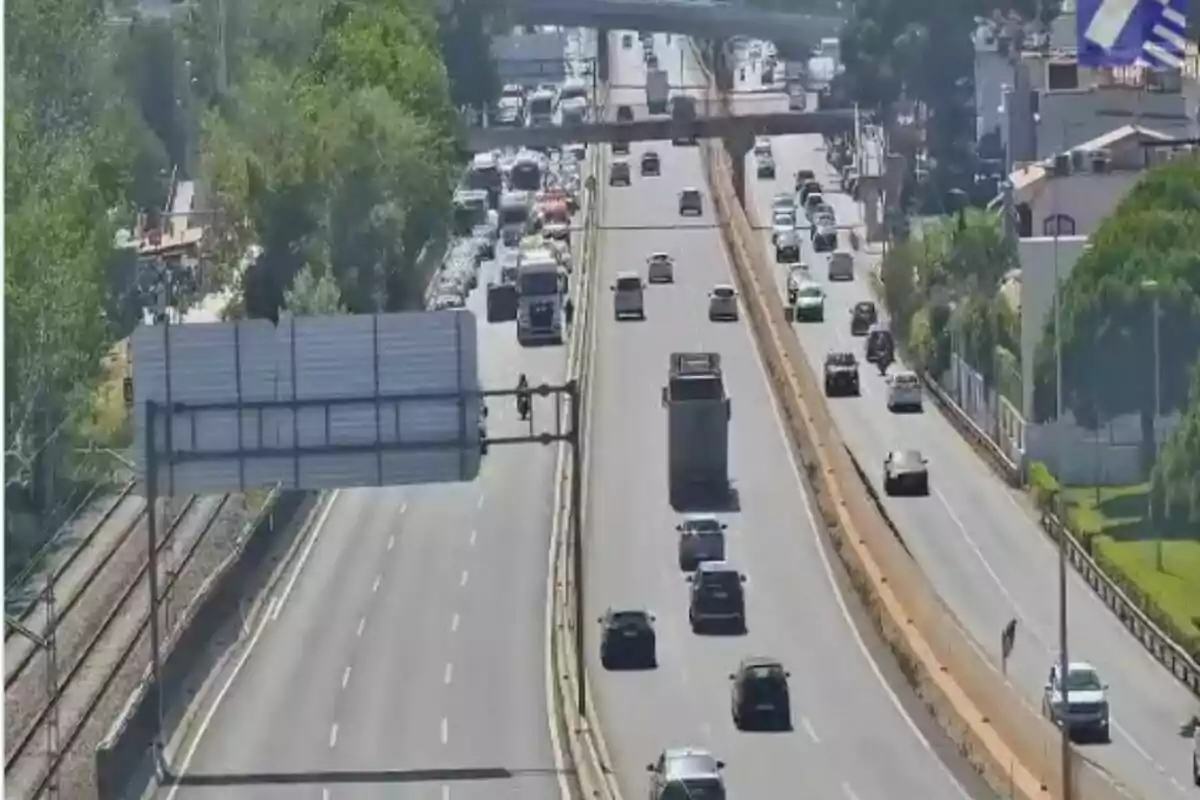 Vista aèria d’una autopista amb diversos carrils on circulen cotxes i camions, amb trànsit més dens en un sentit i arbres als costats.
