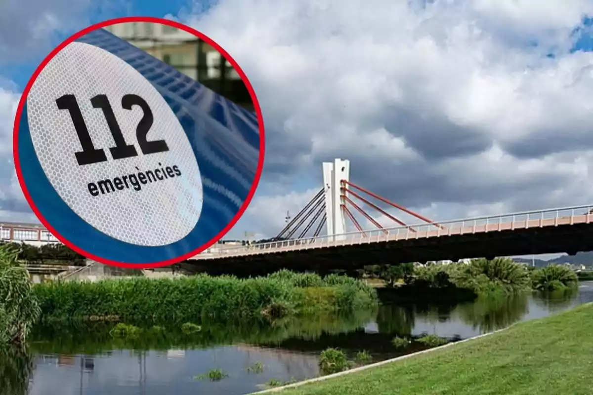 Un pont modern sobre un riu amb un cel ennuvolat i un cercle vermell que destaca el nombre d'emergències 112.