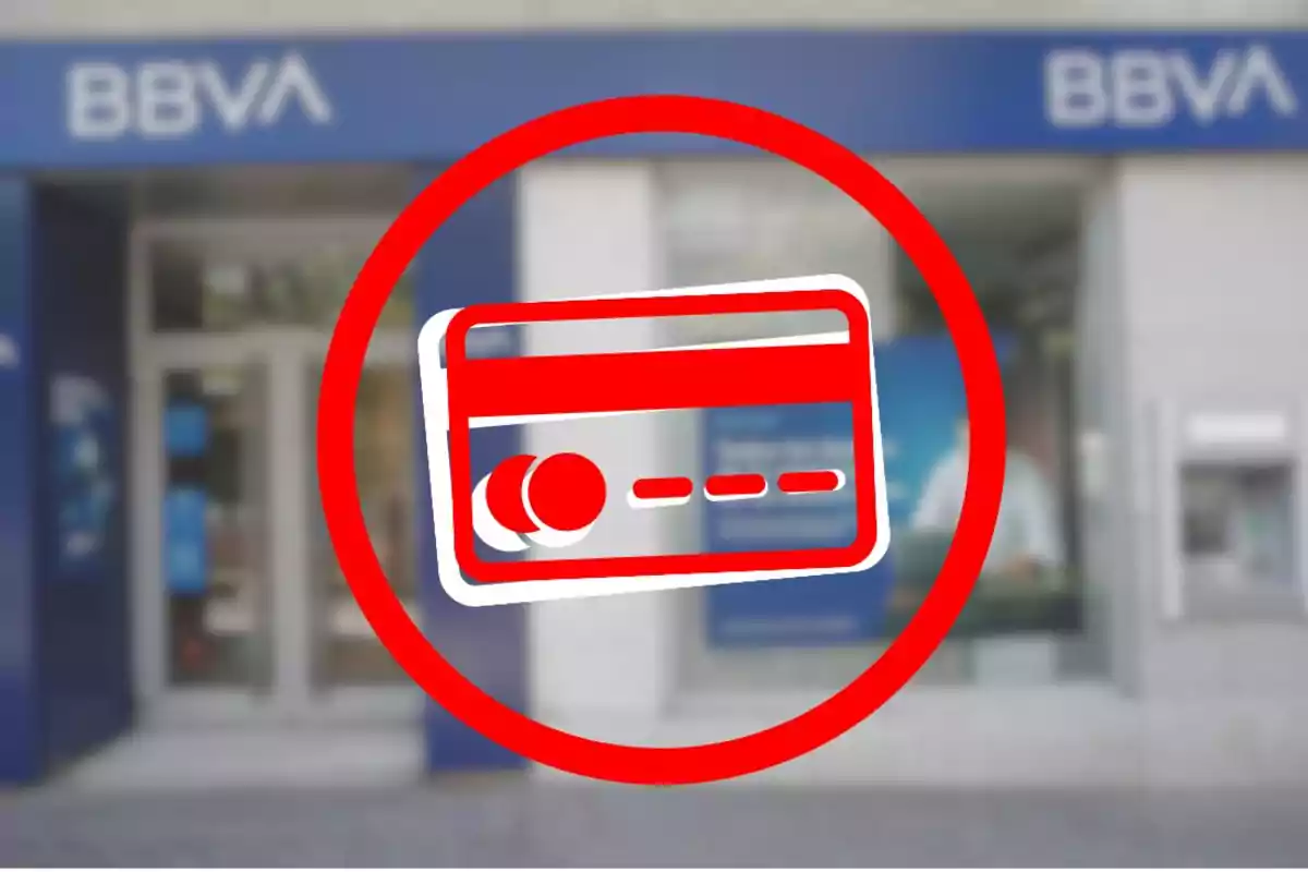 Targeta de crèdit de color vermell dins d’un cercle davant d’una sucursal de BBVA desenfocada