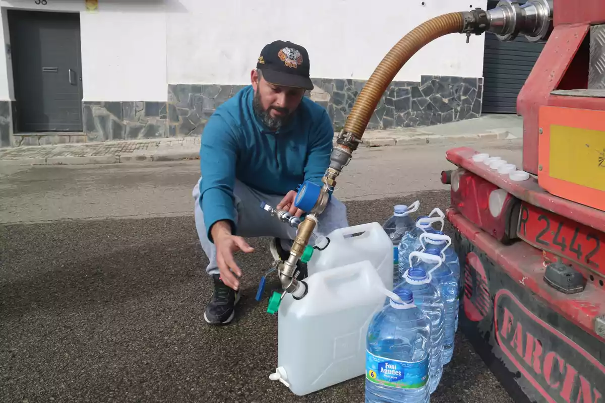 Un hombre llena garrafas de agua desde un camión cisterna en la calle de Vallirana