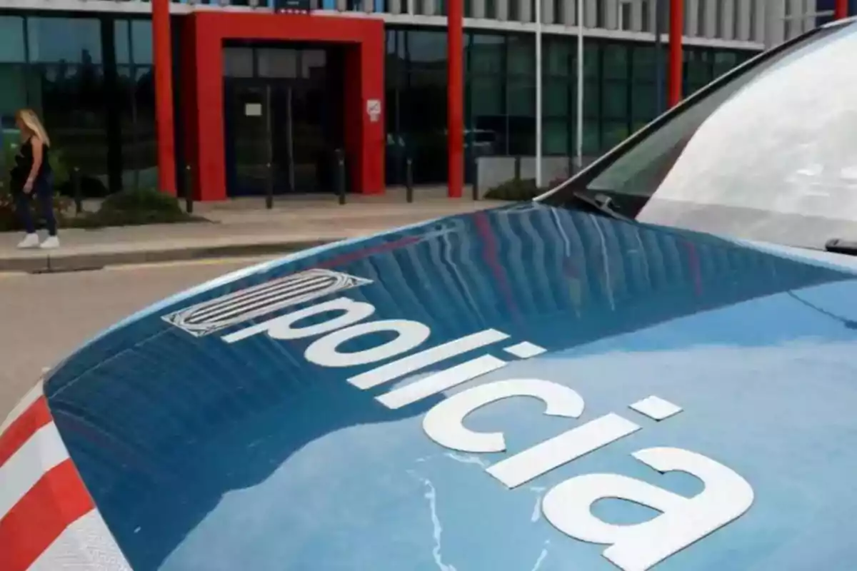 Un coche de policía estacionado frente a un edificio con una persona caminando en el fondo.