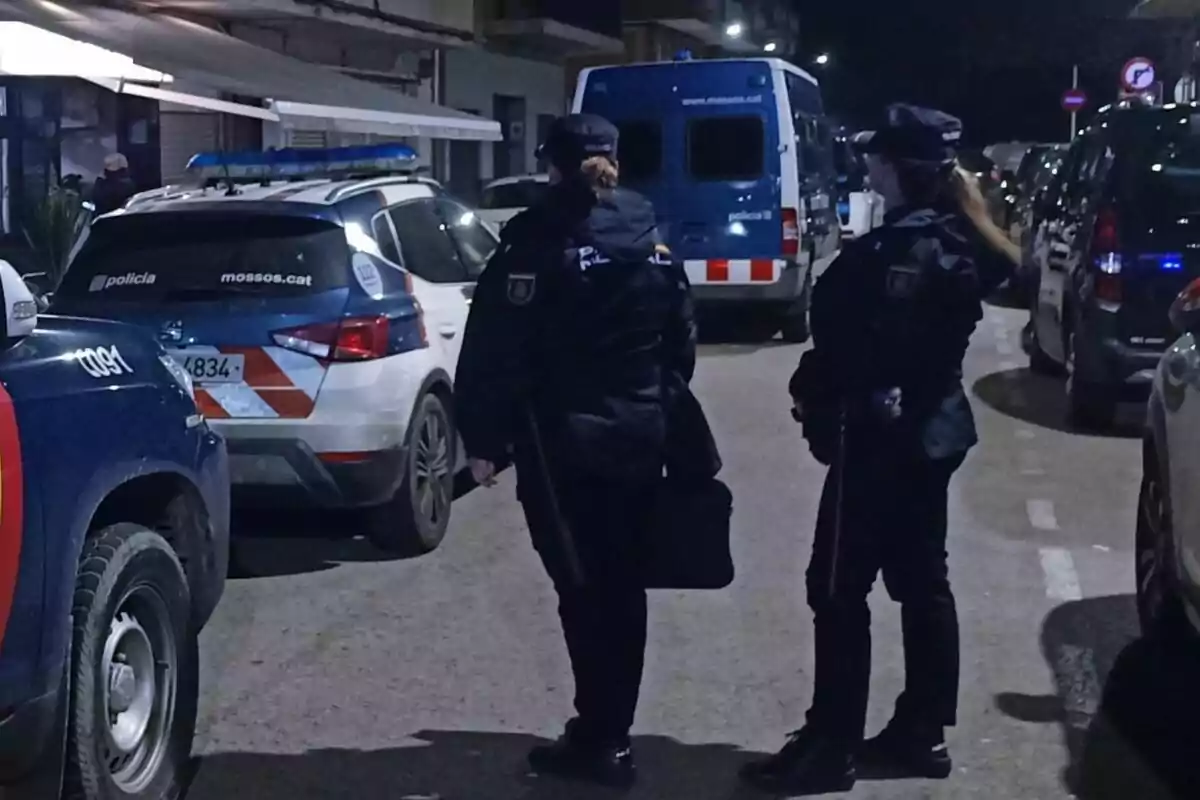 Dos agents de policia drets en un carrer al costat de diversos vehicles policials a la nit.