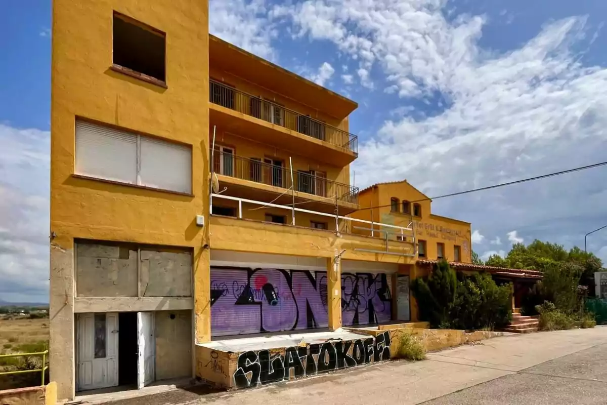 Edifici groc abandonat amb grafits a la façana i cel parcialment ennuvolat.