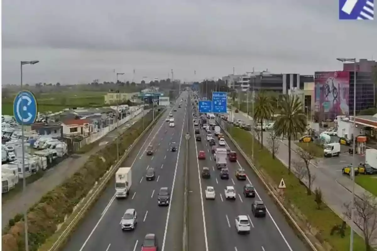 Una carretera de varios carriles con tráfico moderado y edificios al fondo en un día nublado.