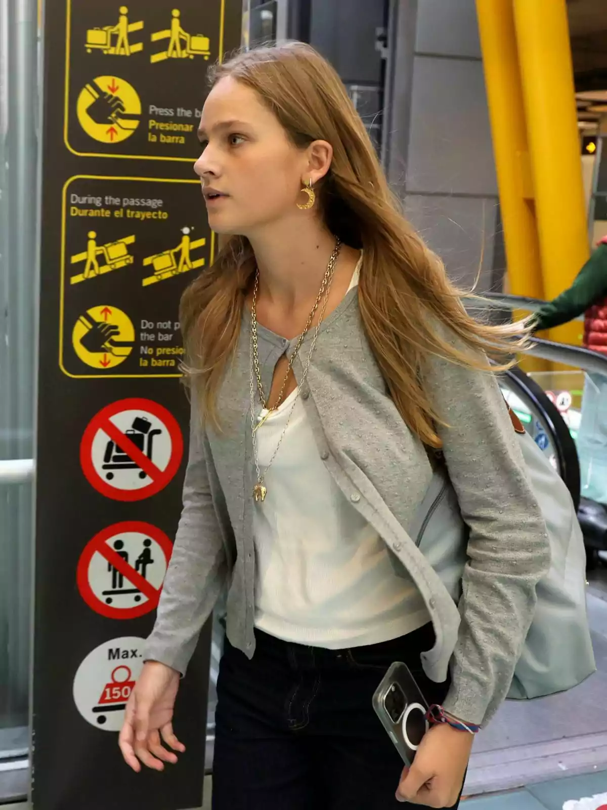 Una noia camina amb una senyalització en un aeroport, portant una motxilla i sostenint un telèfon mòbil a la mà. Una noia camina amb una senyalització en un aeroport, portant una motxilla i sostenint un telèfon mòbil a la mà.