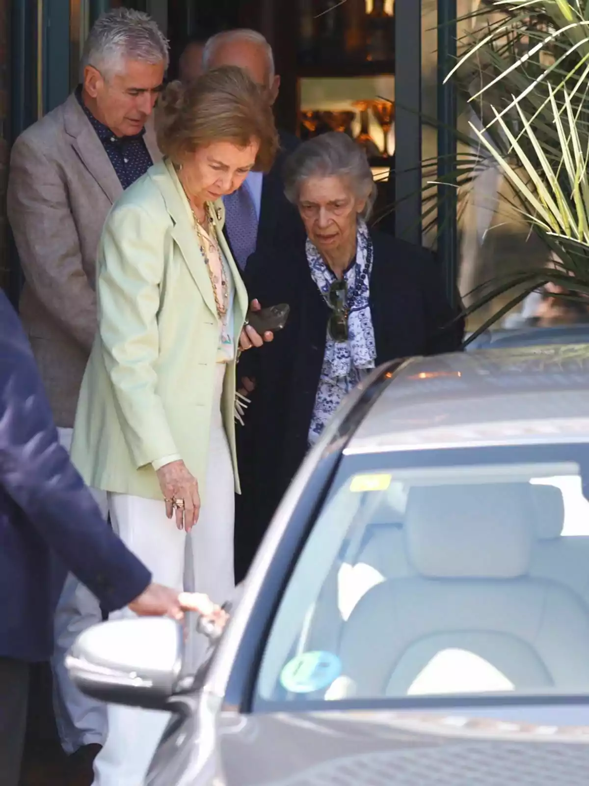 Un grupo de personas mayores sale de un edificio y se dirige hacia un automóvil estacionado cerca.