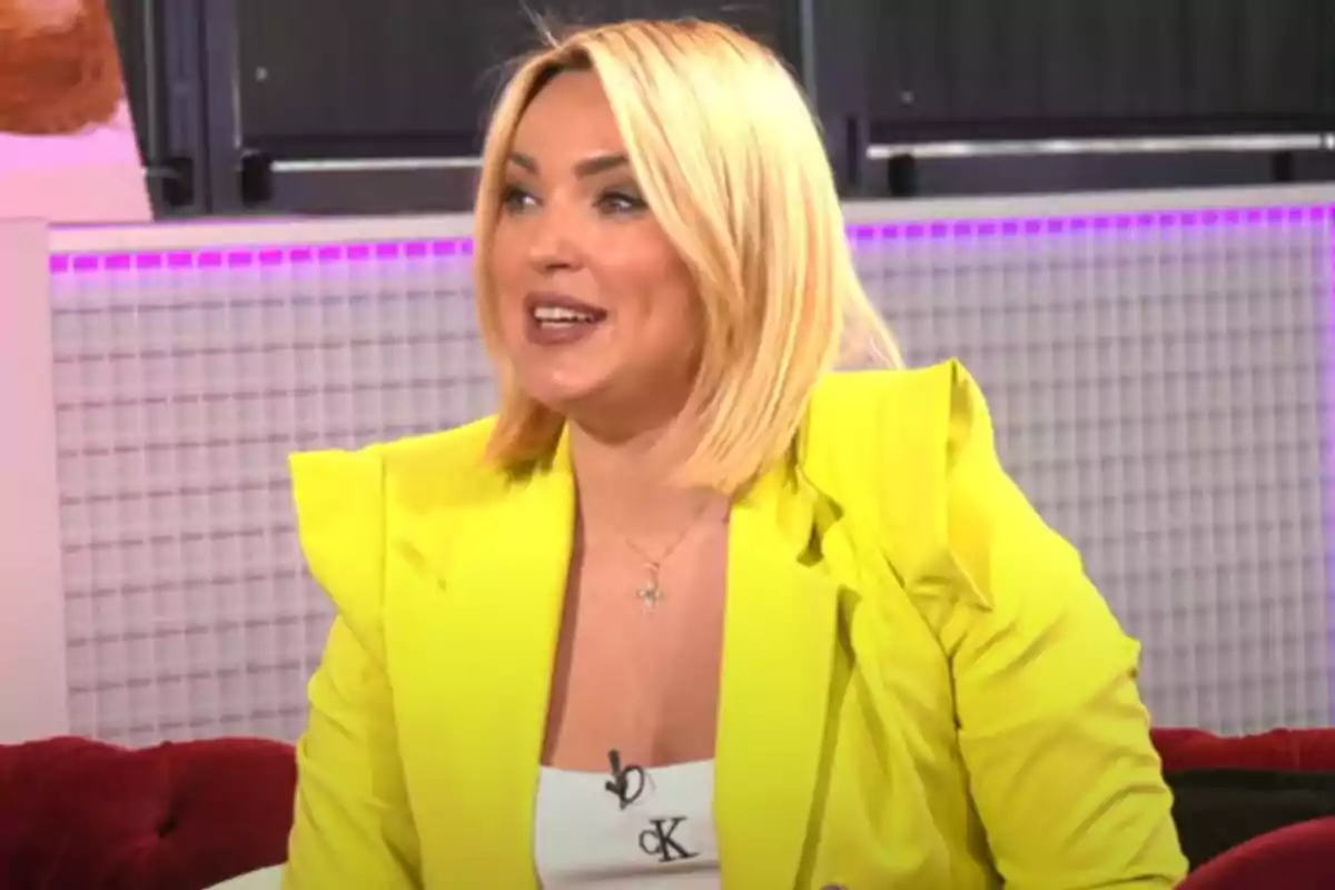 Marta Riesco con cabello rubio y chaqueta amarilla sonríe mientras está sentada en un sofá rojo. Marta Riesco con cabello rubio y chaqueta amarilla sonríe mientras está sentada en un sofá rojo.