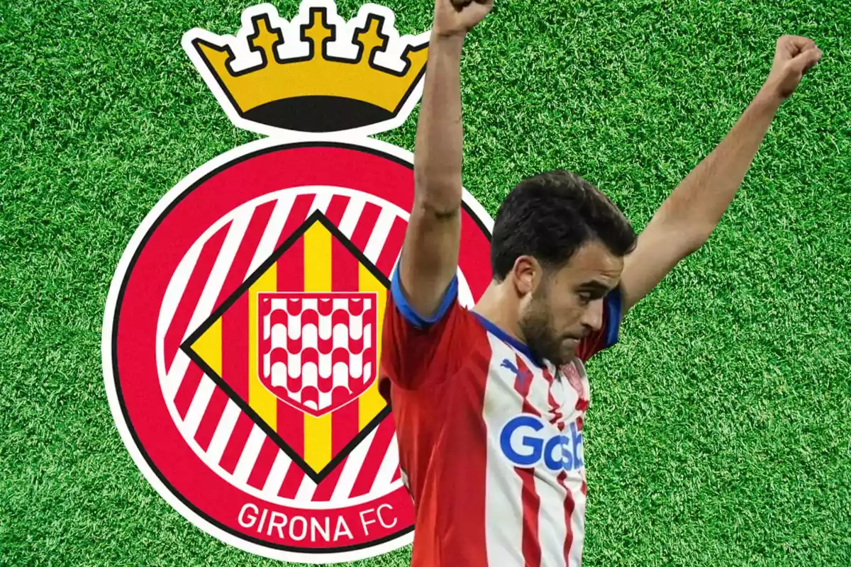 Jugador del Girona FC celebrant amb els braços enlaire davant de l'escut de l'equip sobre un fons de gespa.