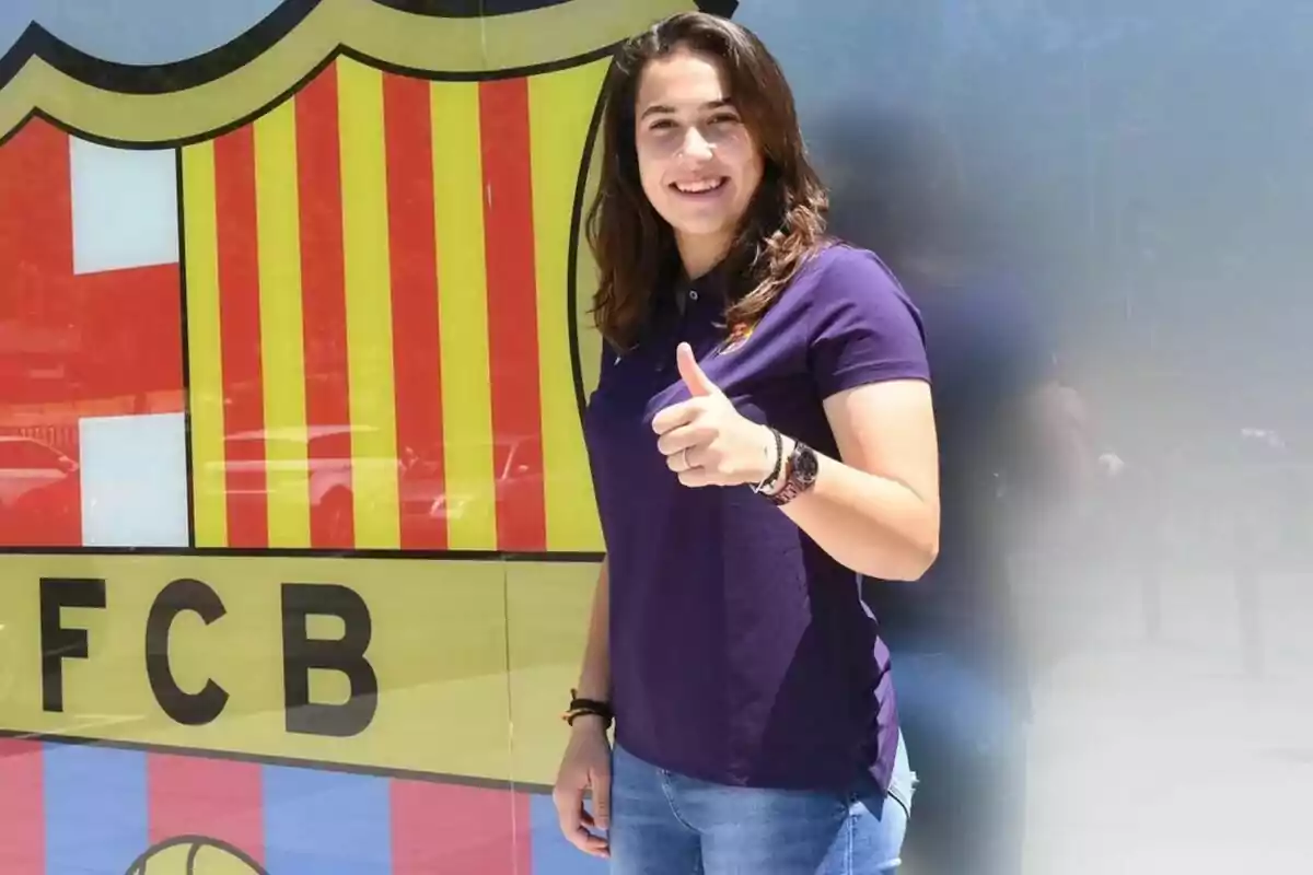 Dona jove somrient i fent el gest de polze amunt davant d’un escut del FC Barcelona Dona jove somrient i fent el gest de polze amunt davant d’un escut del FC Barcelona