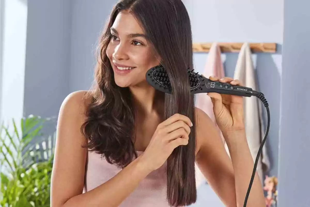Brown woman in pink tank top in bathroom straightening her hair with black electric brush Brown woman in pink tank top in bathroom straightening her hair with black electric brush