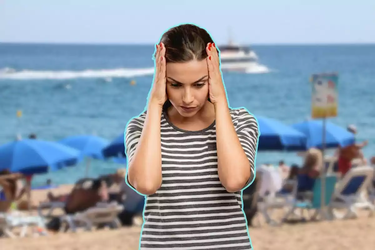 Dona amb samarreta de ratlles sostenint el cap amb les mans en una platja concorreguda.