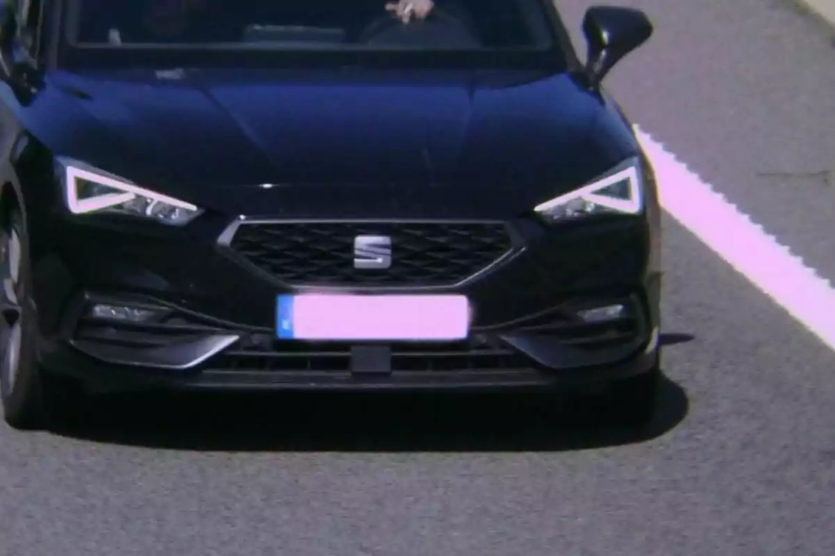 Un coche negro circulando por una carretera con una línea blanca a la derecha.