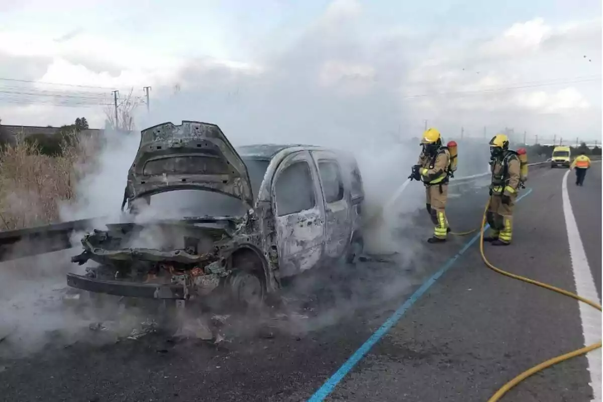 Bombers apagant un incendi en un vehicle en una carretera.