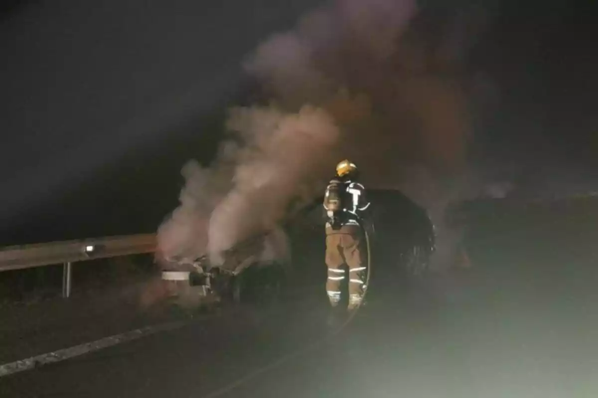 Bombero apagando un incendio en un vehículo en la carretera durante la noche.