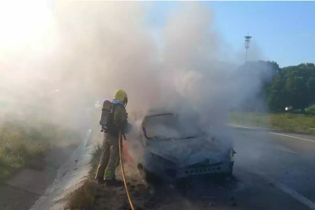 Bomber apagant un incendi en un automòbil en una carretera amb molt de fum al voltant.