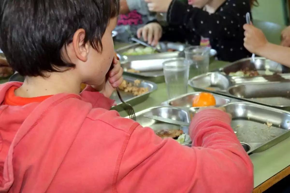 Un nen, d'esquena, menjant al menjador escolar