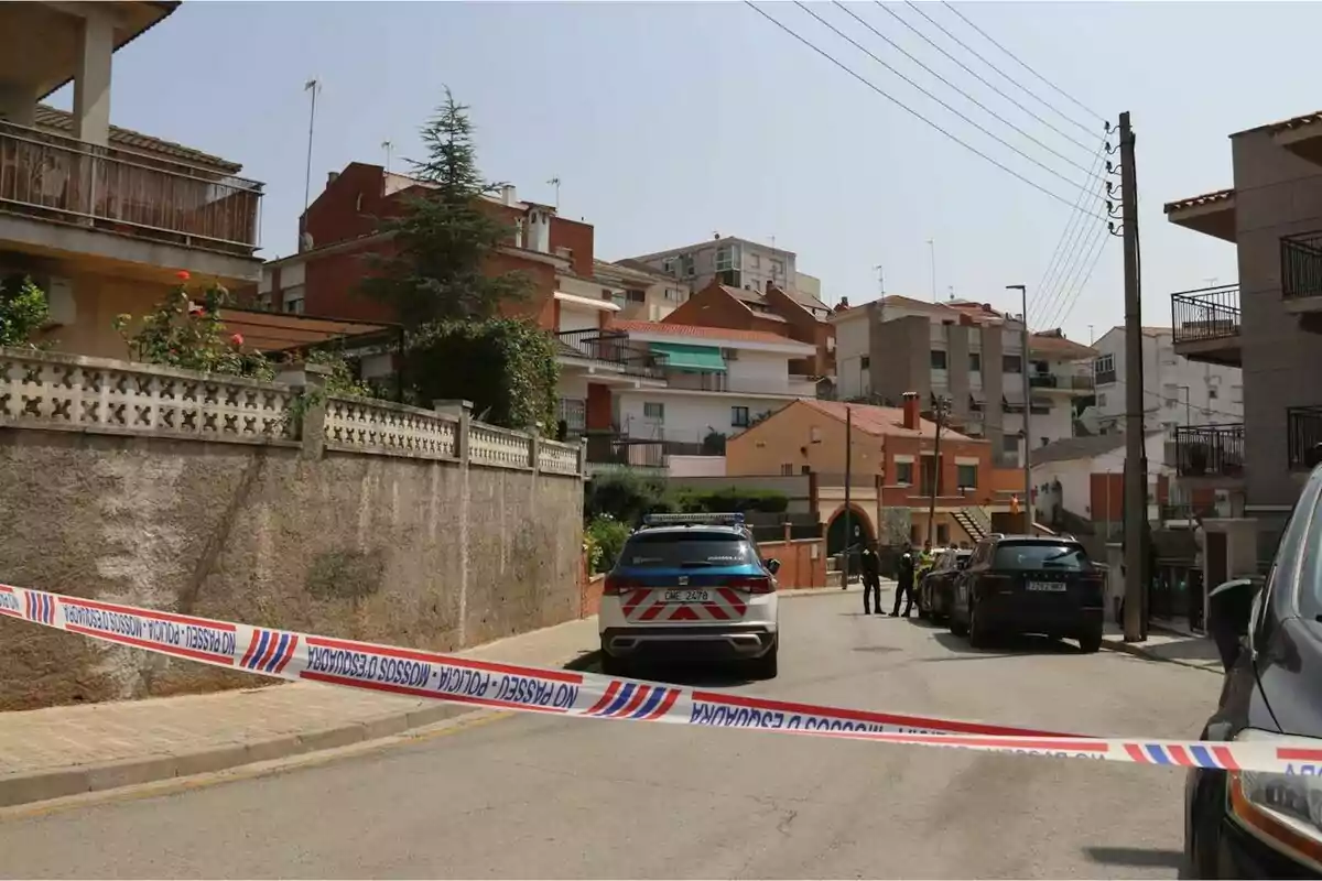 Carrer residencial acordonat per la policia amb diversos vehicles i edificis al fons.