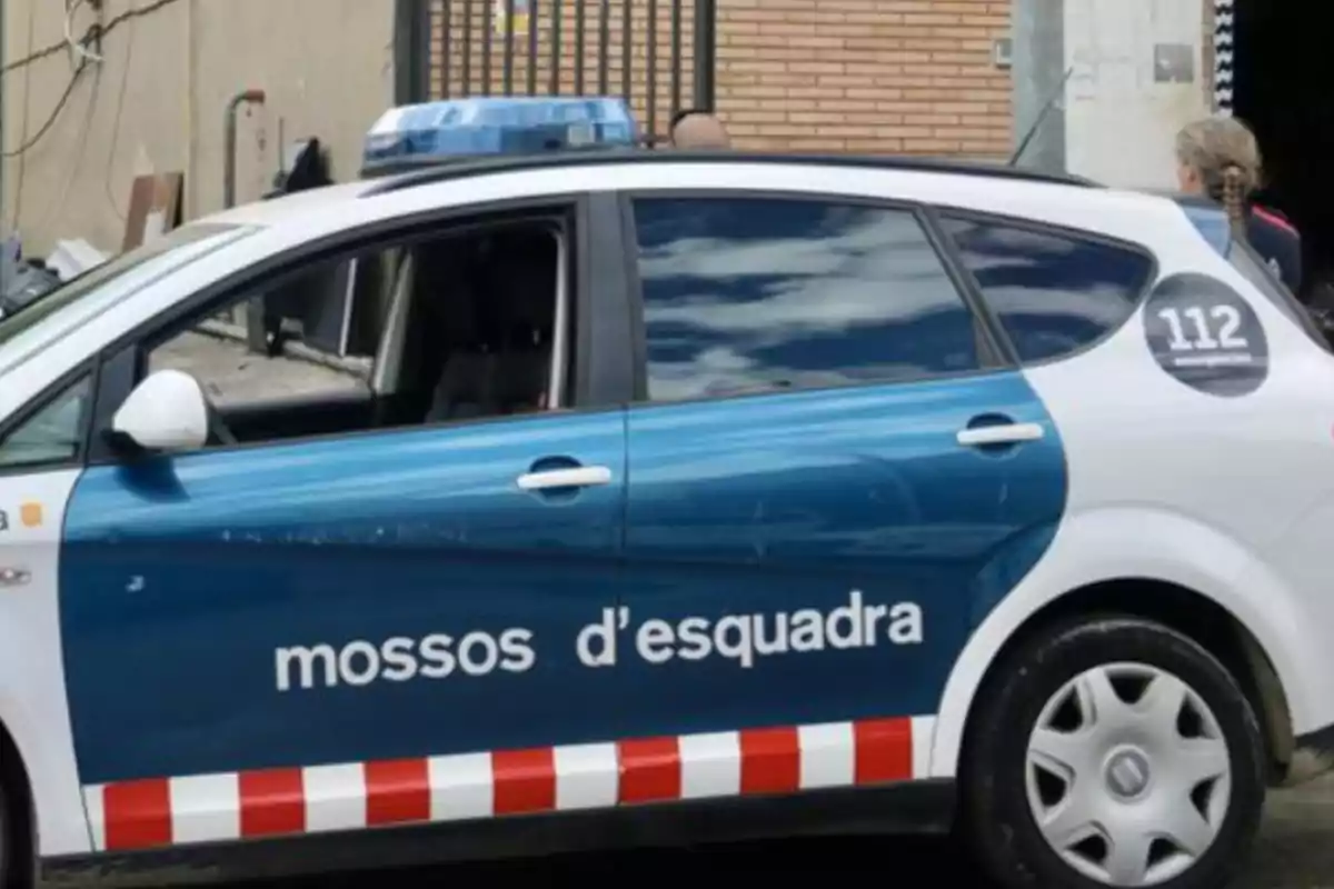 Un coche de los Mossos d'Esquadra estacionado junto a un edificio con una persona cerca.