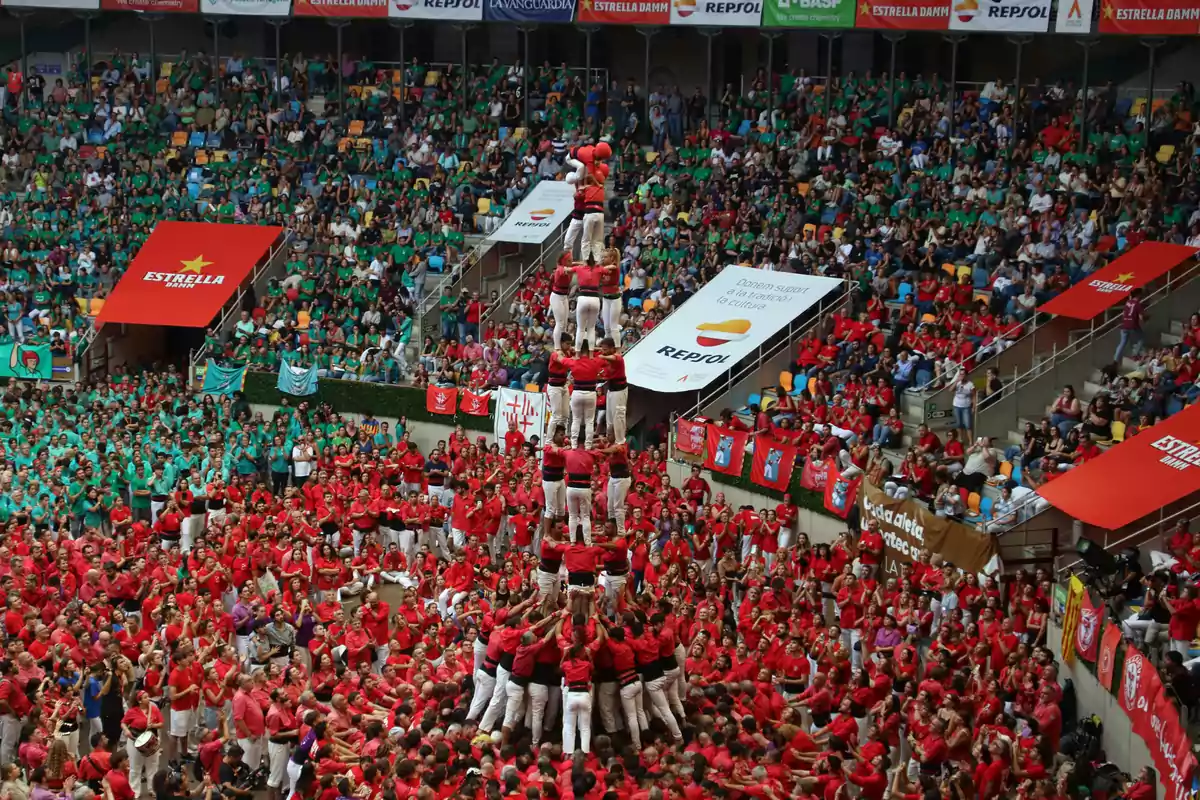 Un grupo de personas vestidas de rojo y blanco forma una torre humana en un estadio lleno de espectadores.