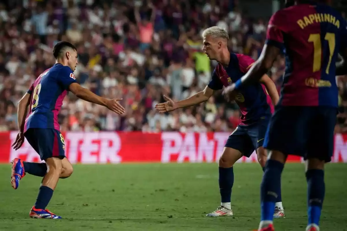 Jugadors de futbol celebrant al camp amb una encaixada de mans mentre un altre jugador s'acosta.