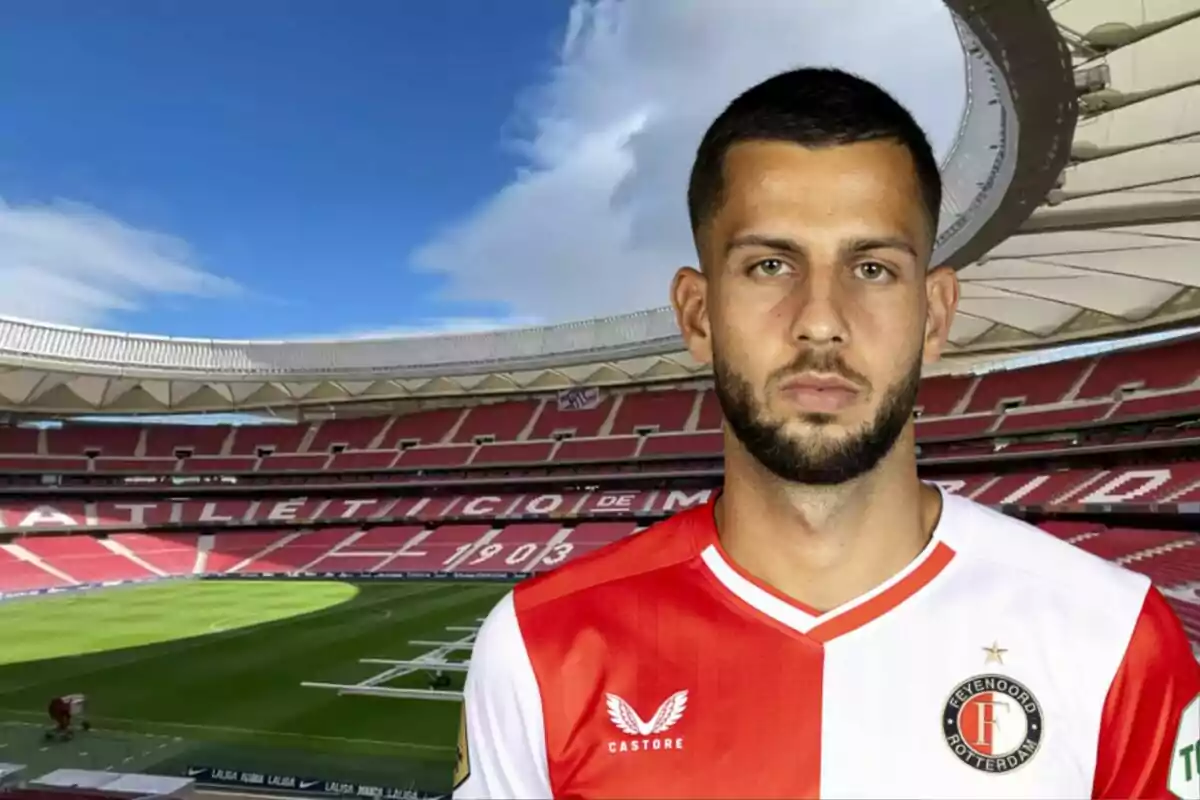 Un jugador de fútbol con la camiseta del Feyenoord Rotterdam posando frente a un estadio de fútbol vacío.