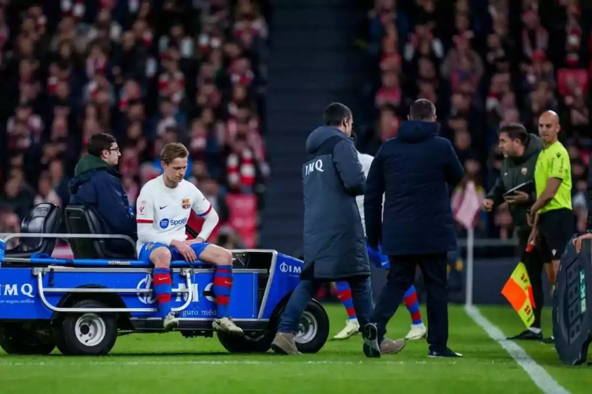 Jugador del FC Barcelona siendo retirado del campo en un carrito médico durante un partido.