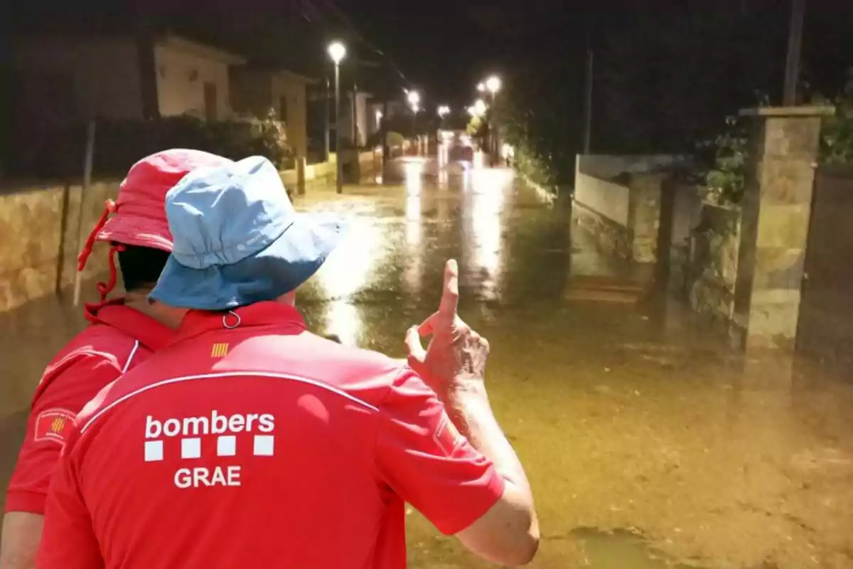 Dos bombers amb barrets observen un carrer inundat a la nit.