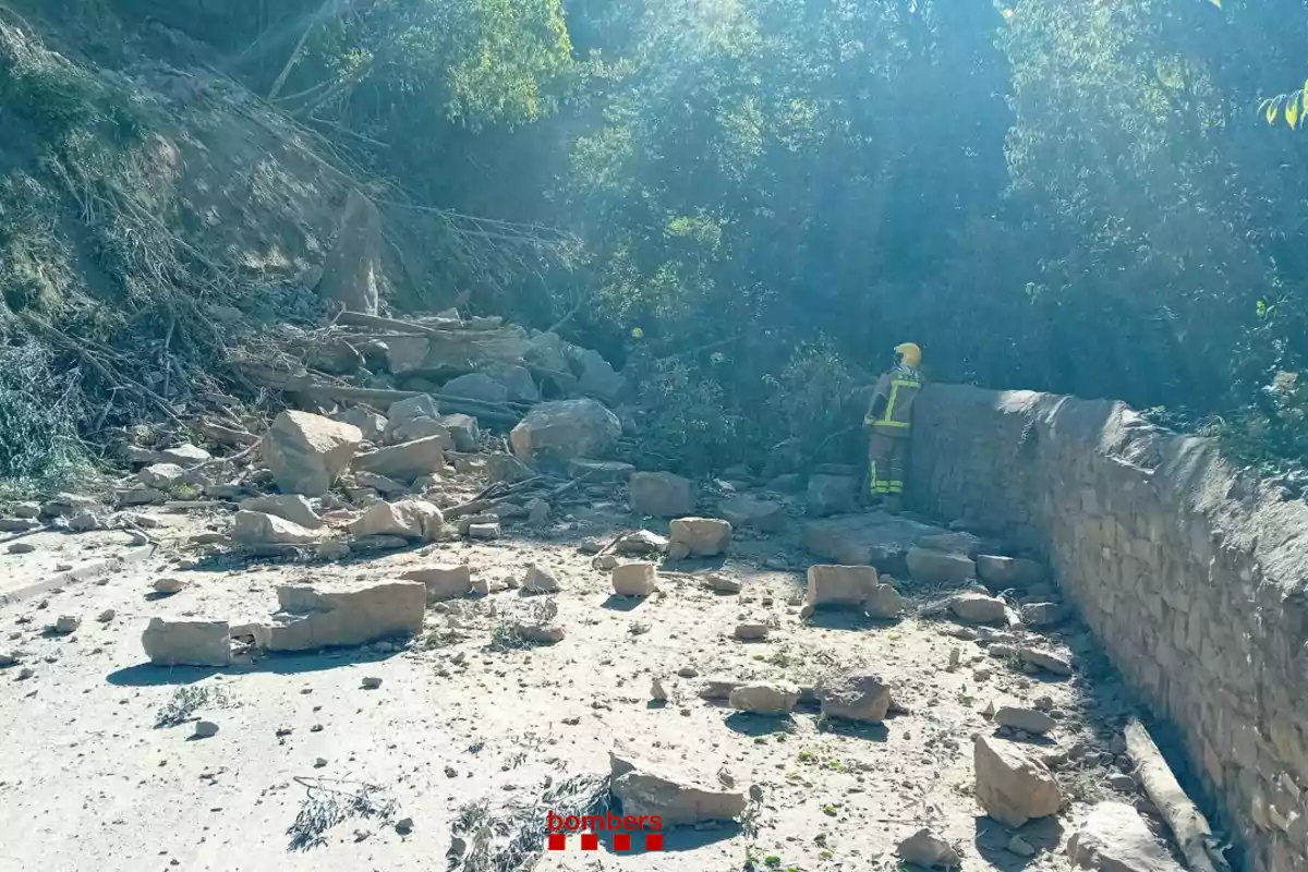 Un deslizamiento de tierra bloquea un camino con rocas y escombros mientras un bomber evalúa la situación