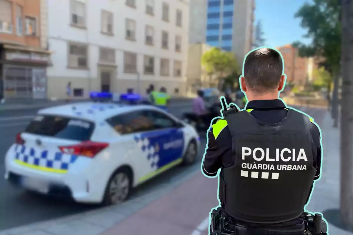 Un agent de la policia urbana d'esquena, amb una armilla que diu "Policia Guàrdia Urbana", observa una escena al carrer on hi ha un cotxe patrulla estacionat i altres agents al fons.