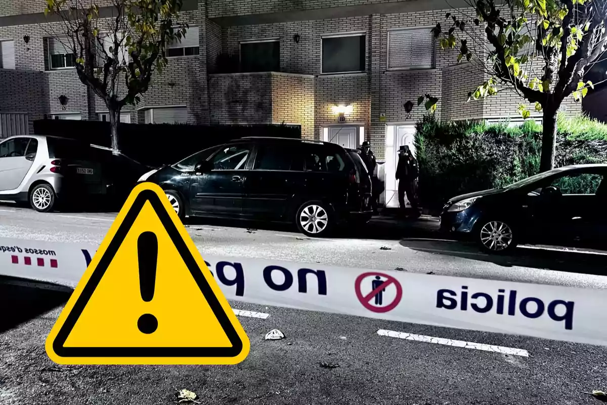 Cinta de policia bloqueja l'accés a un carrer on s'observa un cotxe negre estacionat davant d'un edifici residencial amb llums encesos i dues persones a l'entrada.