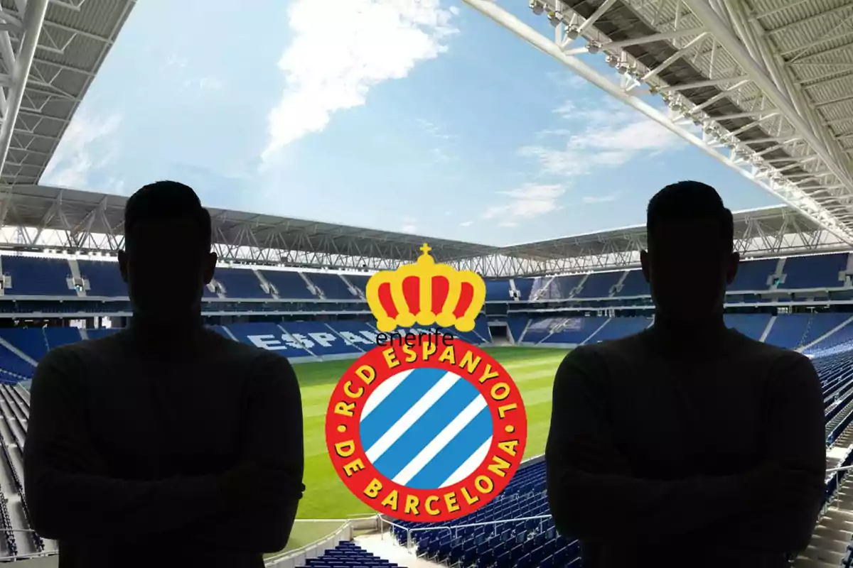 Dues persones amb siluetes fosques posen davant de l'escut del RCD Espanyol de Barcelona en un estadi de futbol buit.