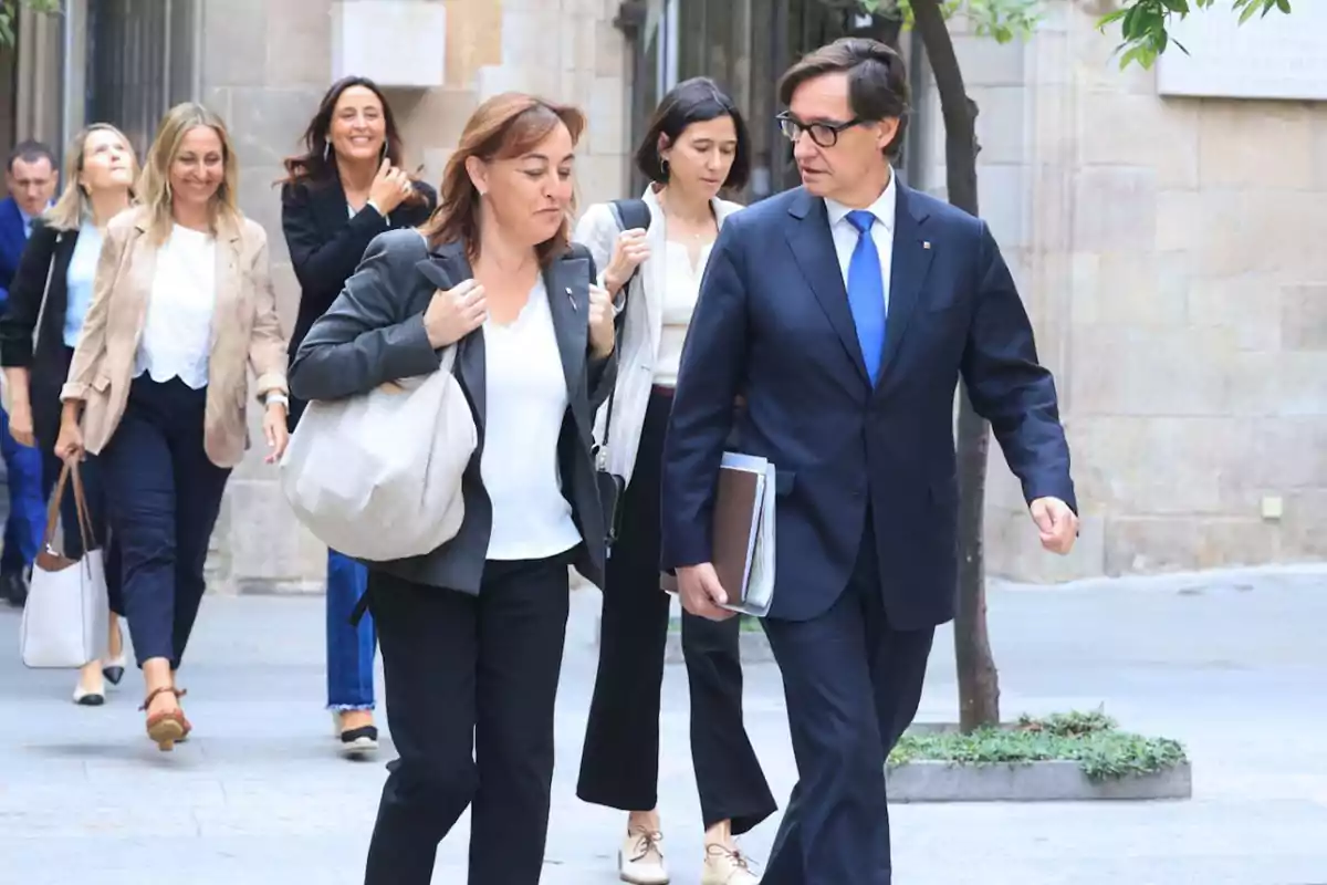 Un grupo de personas caminando por una calle, algunas de ellas llevan carpetas y bolsos.