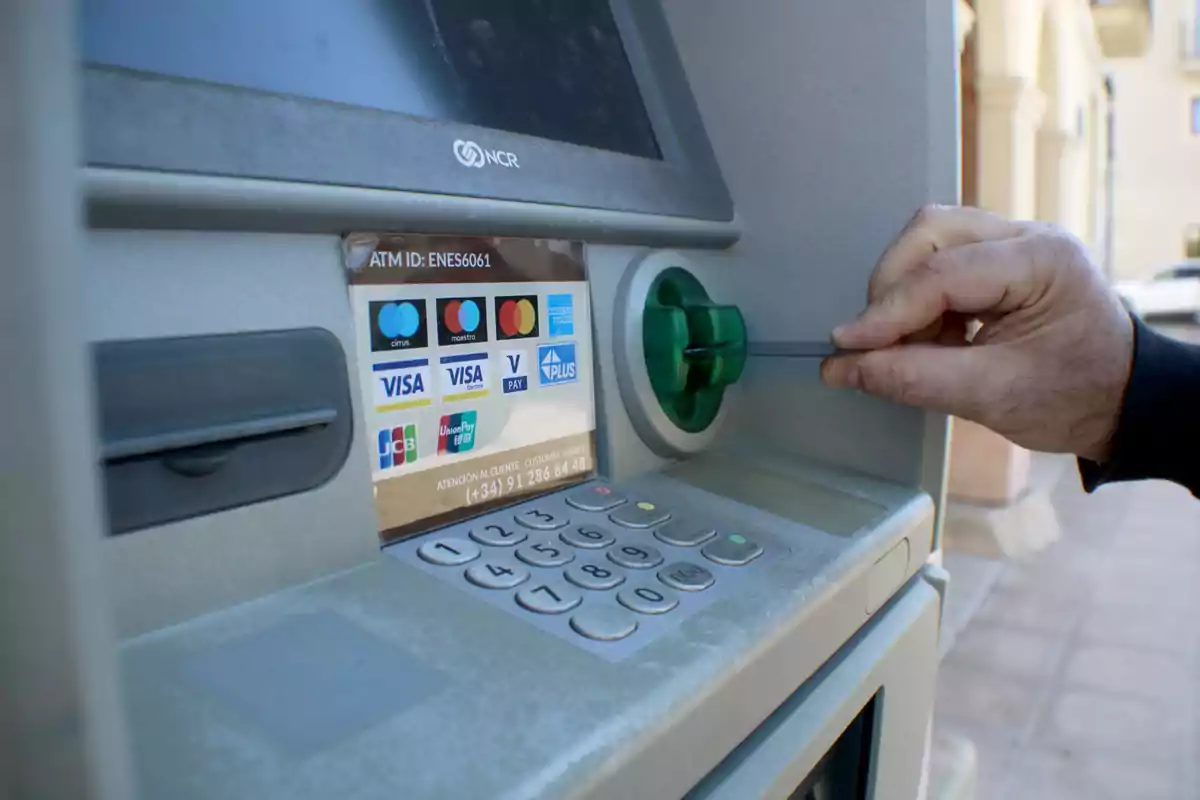 Persona inserint una targeta en un caixer automàtic amb logotips de diverses targetes de crèdit i dèbit.