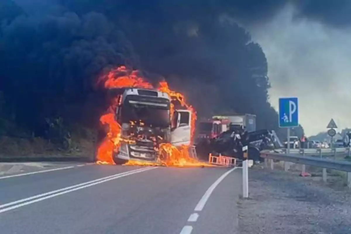 Un camió en flames en una carretera amb fum negre elevant-se al cel.