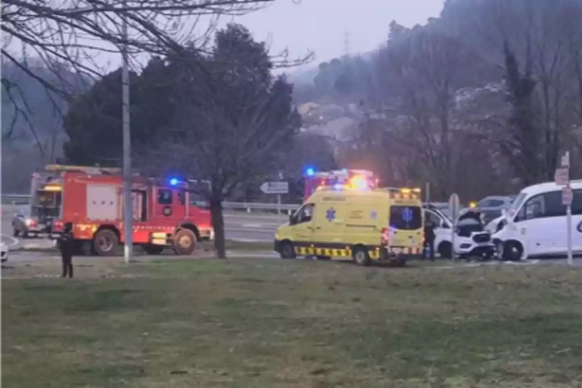 Un camió de bombers i una ambulància són a l'escena d'un accident de trànsit en una carretera envoltada d'arbres i turons.