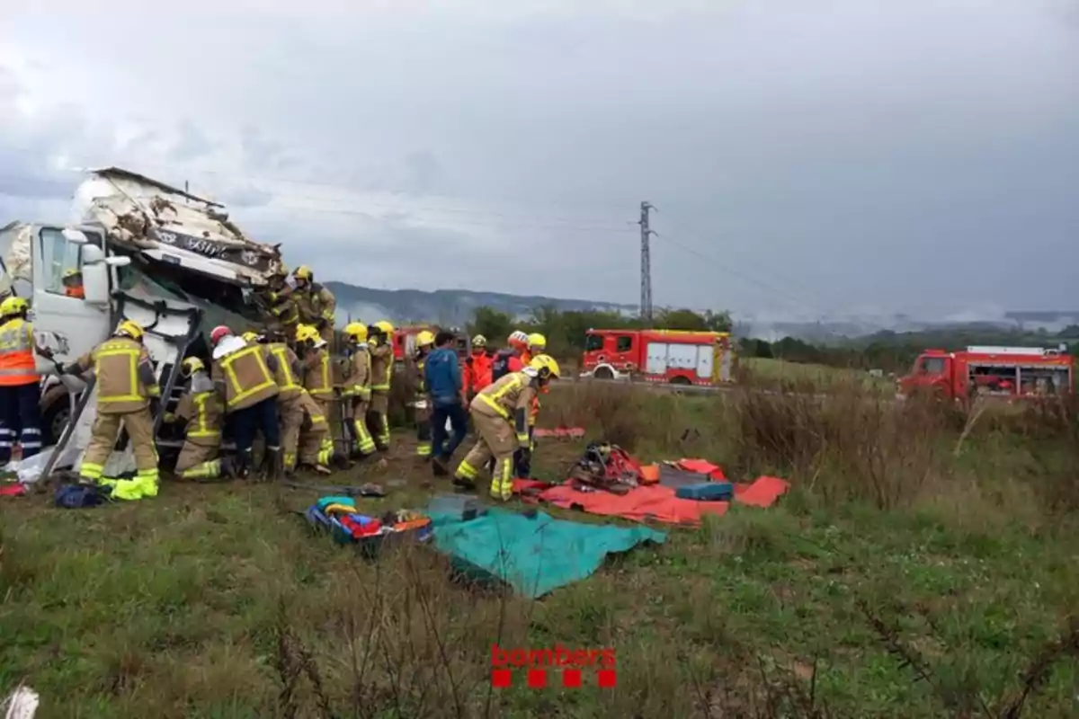 Bomberos trabajando en el rescate de un accidente de camión en un campo con vehículos de emergencia en el fondo.