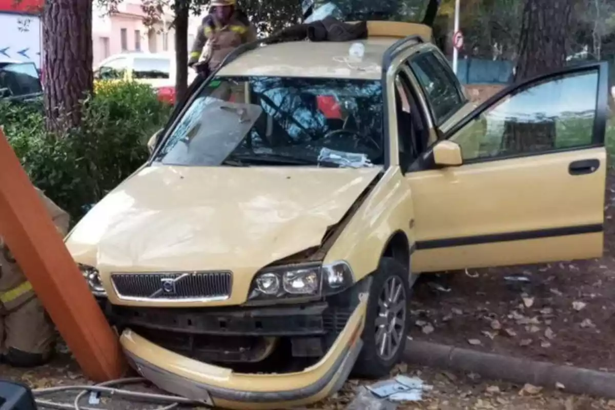 Un coche amarillo chocado contra un poste con la puerta delantera abierta y un bombero cerca.