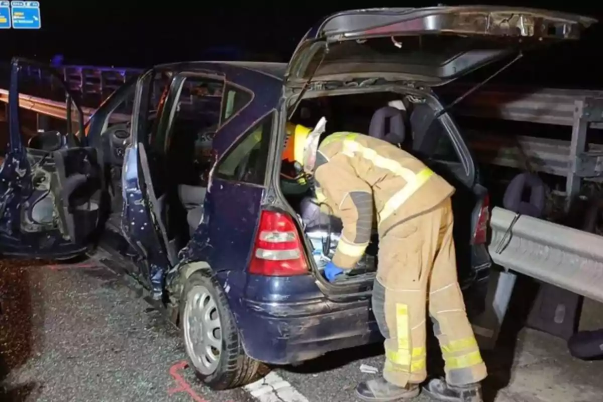 Un bombero revisa el maletero de un coche dañado en un accidente nocturno en la carretera.