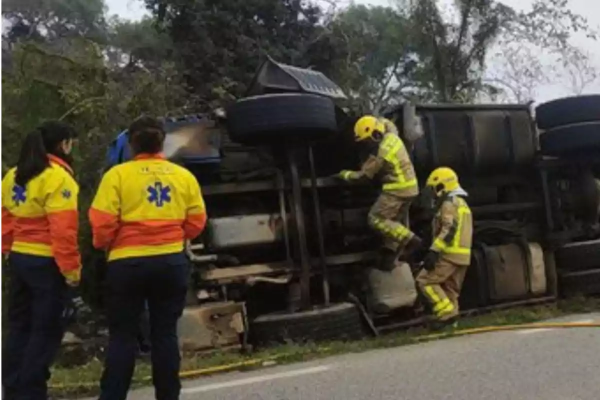 Personal de emergencia y bomberos trabajando en el lugar de un camión volcado en la carretera.