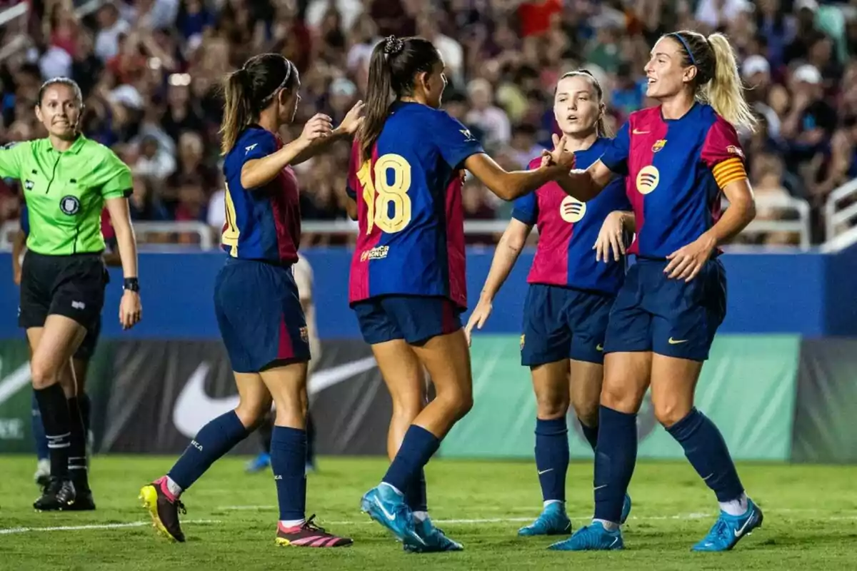 Jugadores de futbol celebren al camp mentre una àrbitre observa.