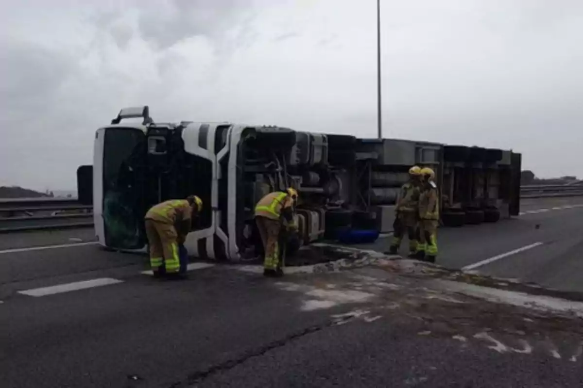 Un camió bolcat a la carretera amb bombers treballant al lloc.