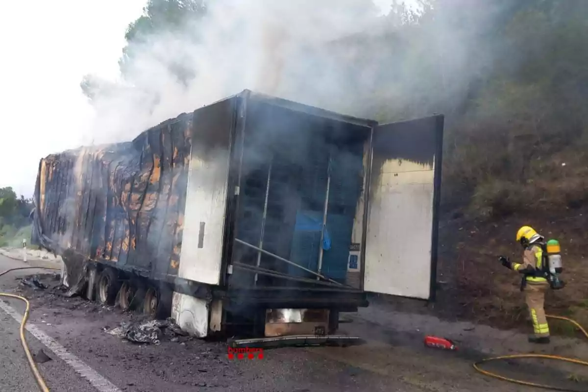 Un camión incendiado en la carretera mientras un bombero trabaja para controlar el fuego.