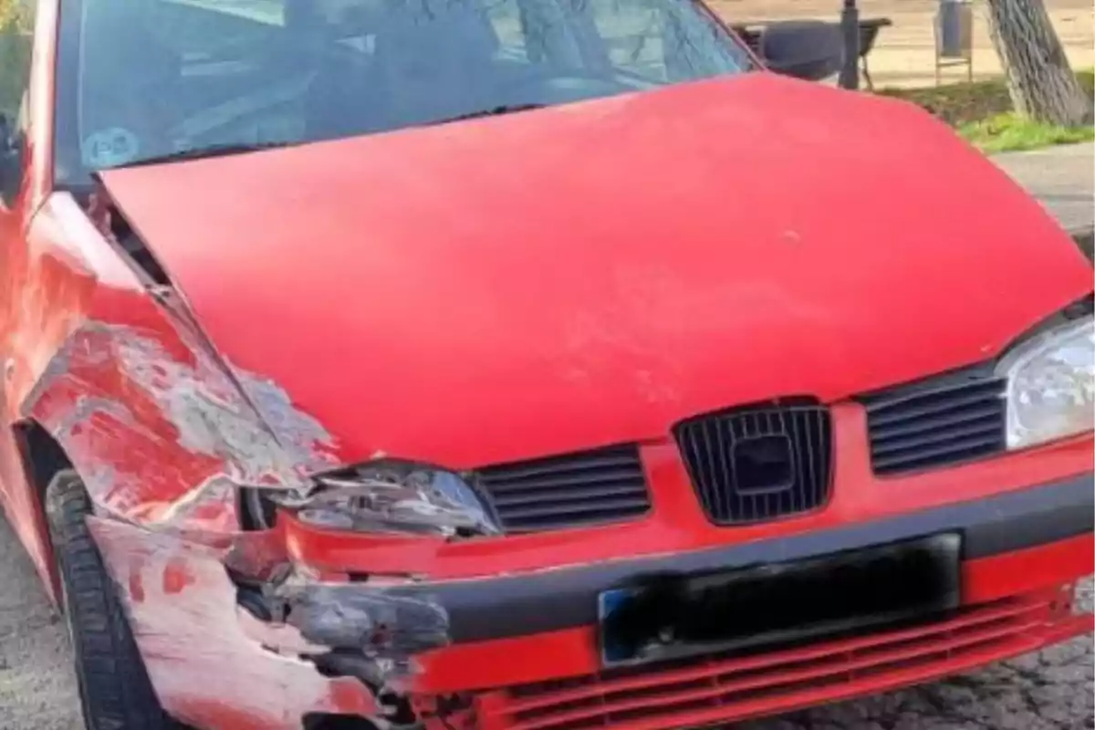 Un coche rojo con el parachoques delantero dañado y abolladuras en el lado izquierdo.