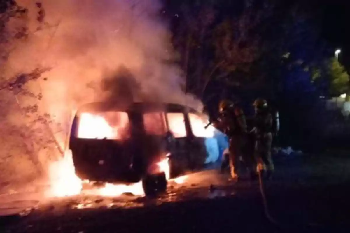 Bomberos apagando un incendio en un vehículo en llamas durante la noche.