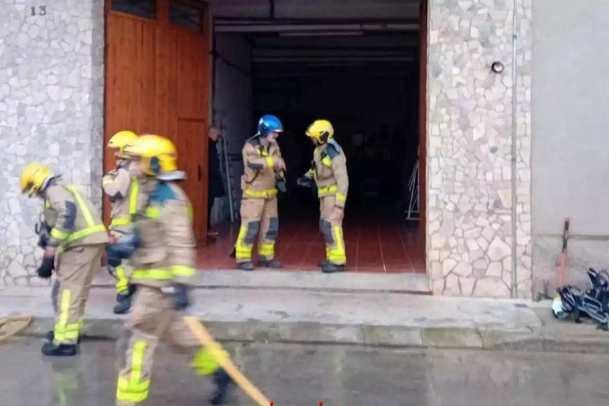 Bombers amb cascos grocs i blaus són davant d'un edifici de pedra, alguns sostenen una mànega.