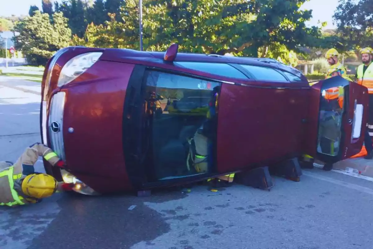 Un cotxe bolcat de costat a la carretera amb bombers treballant al voltant.