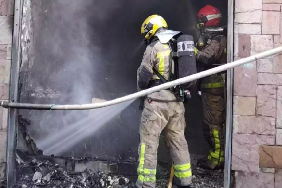 Bombers combatent un incendi a un edifici amb mànegues d'aigua.