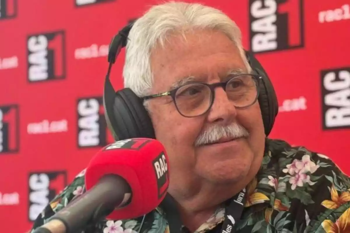 Home gran amb ulleres i auriculars parlant davant d’un micròfon vermell en un estudi de ràdio amb un fons de logotips de RAC1