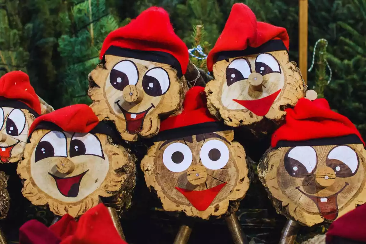 Un grupo de figuras de madera con caras sonrientes pintadas y gorros rojos.