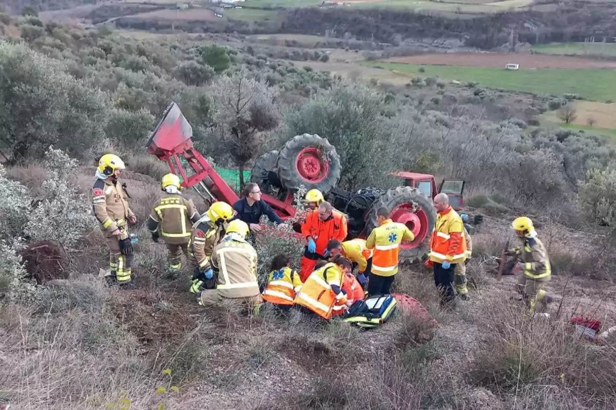 Un grupo de bomberos y personal de emergencia atiende una situación en un campo donde un tractor se ha volcado.